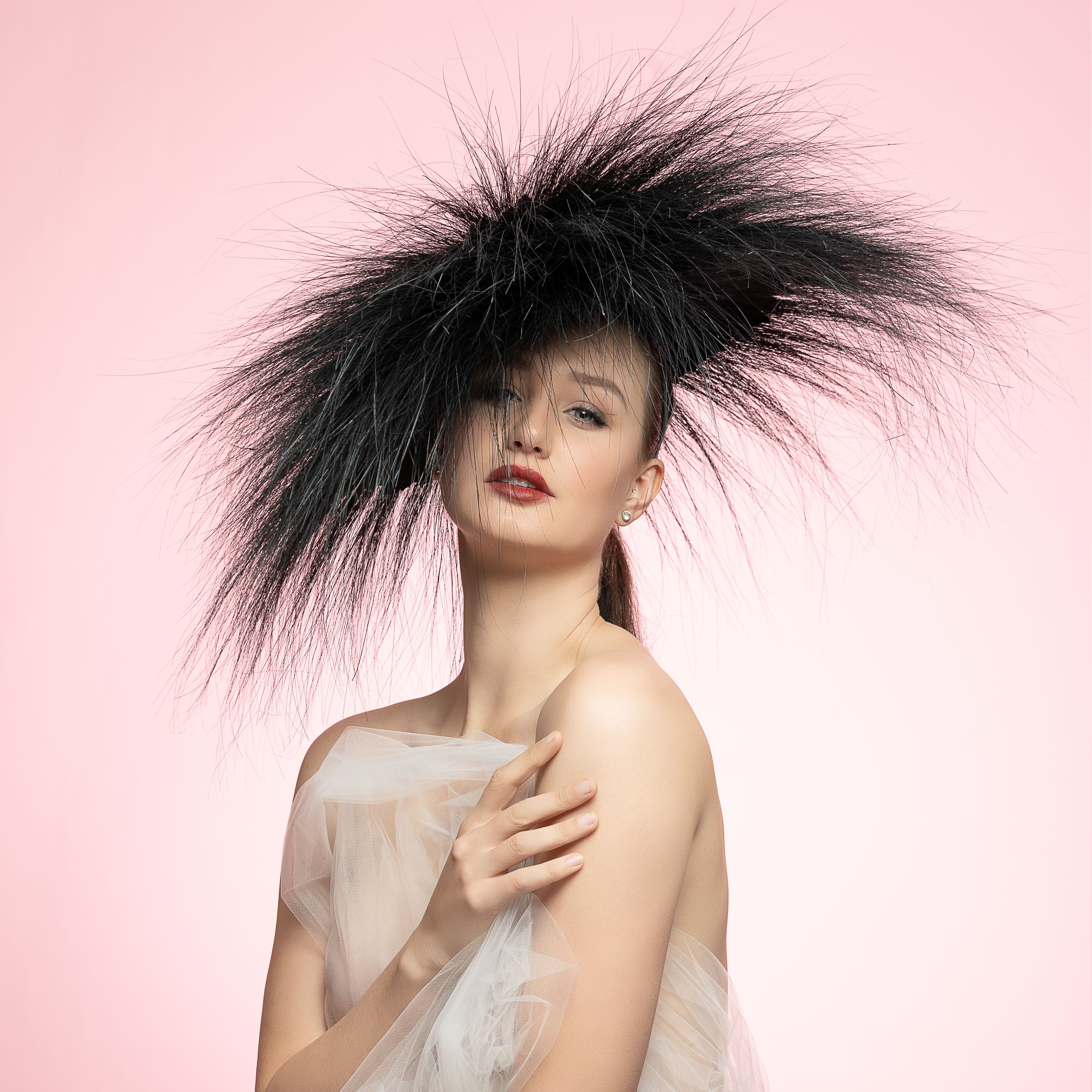 Woman wearing a large black feathered headpiece against a pink background