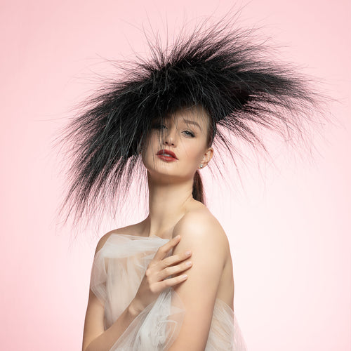 Woman wearing a large black feathered headpiece against a pink background