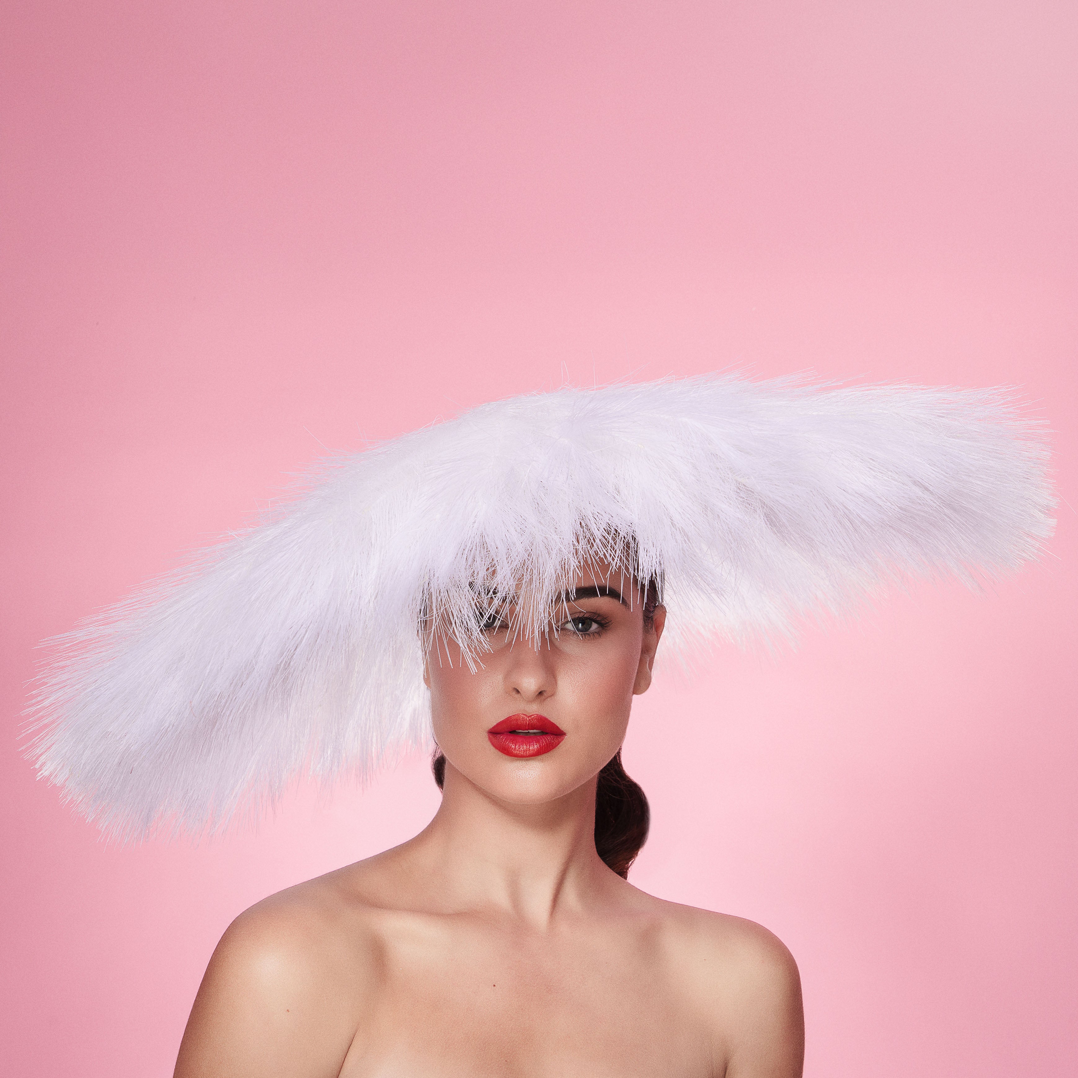 Woman wearing a large white feathered hat against a pink background