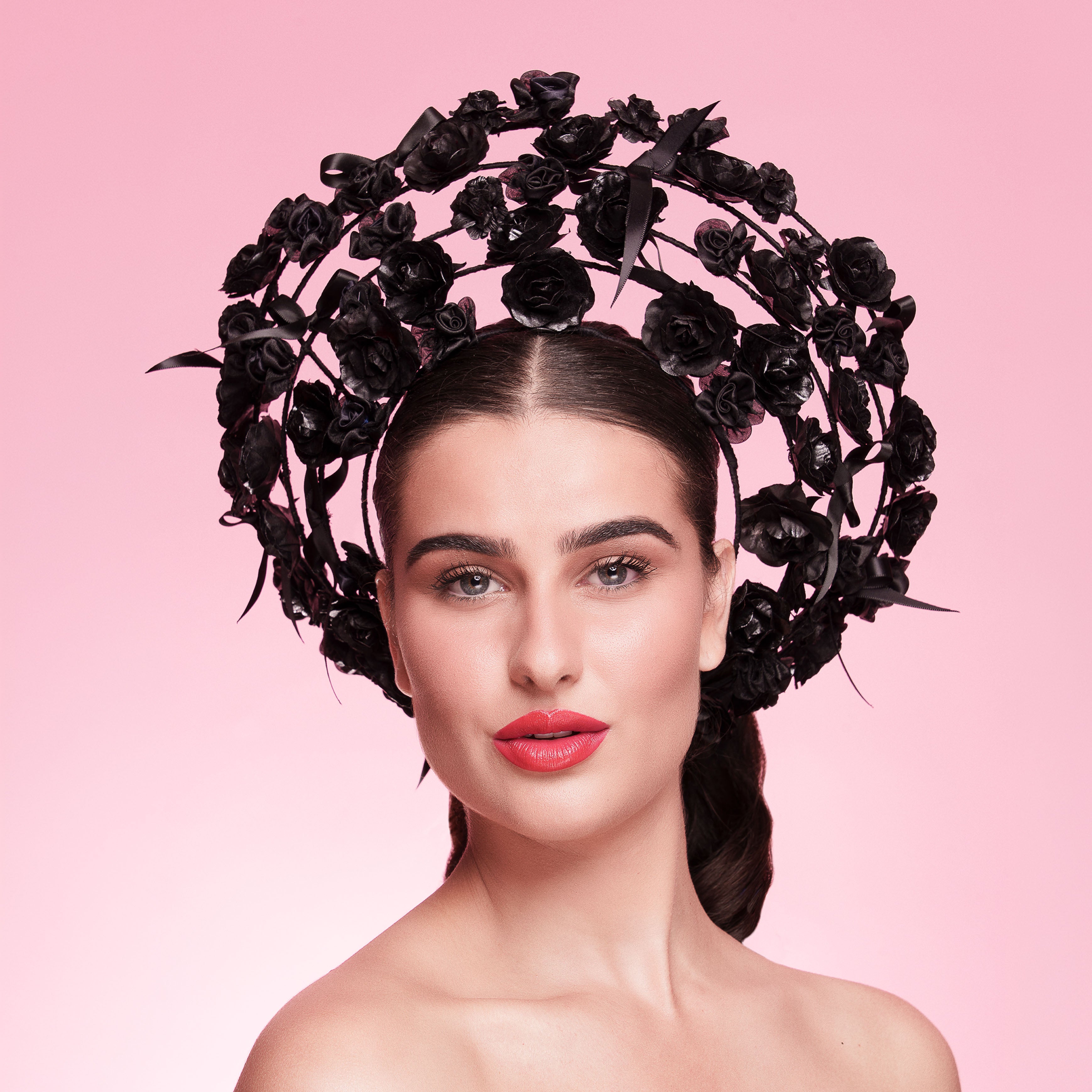 Woman with a headpiece made of black roses on a pink background