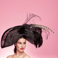 Woman wearing a decorative black hat with feathers against a pink background