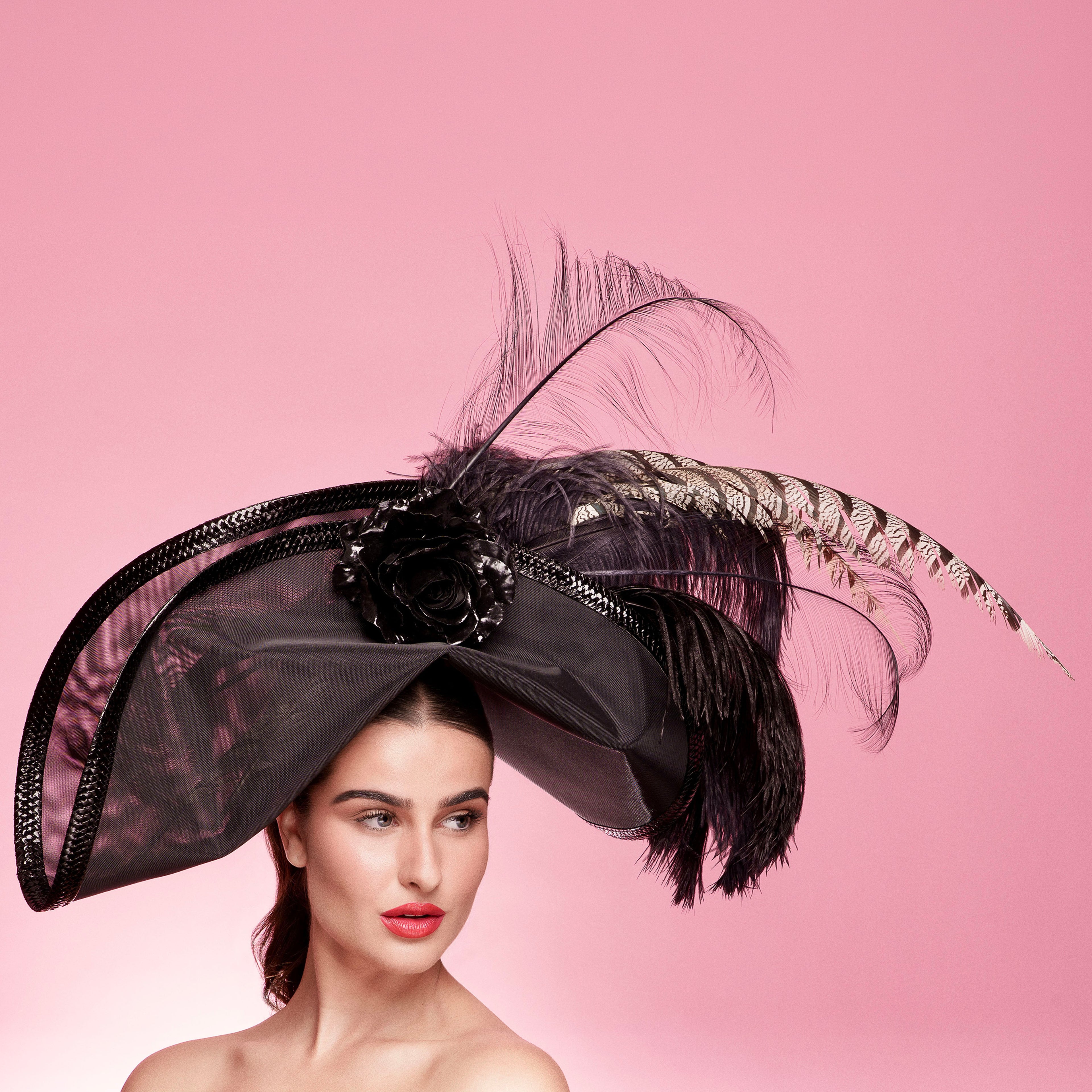 Woman wearing a decorative black hat with feathers against a pink background