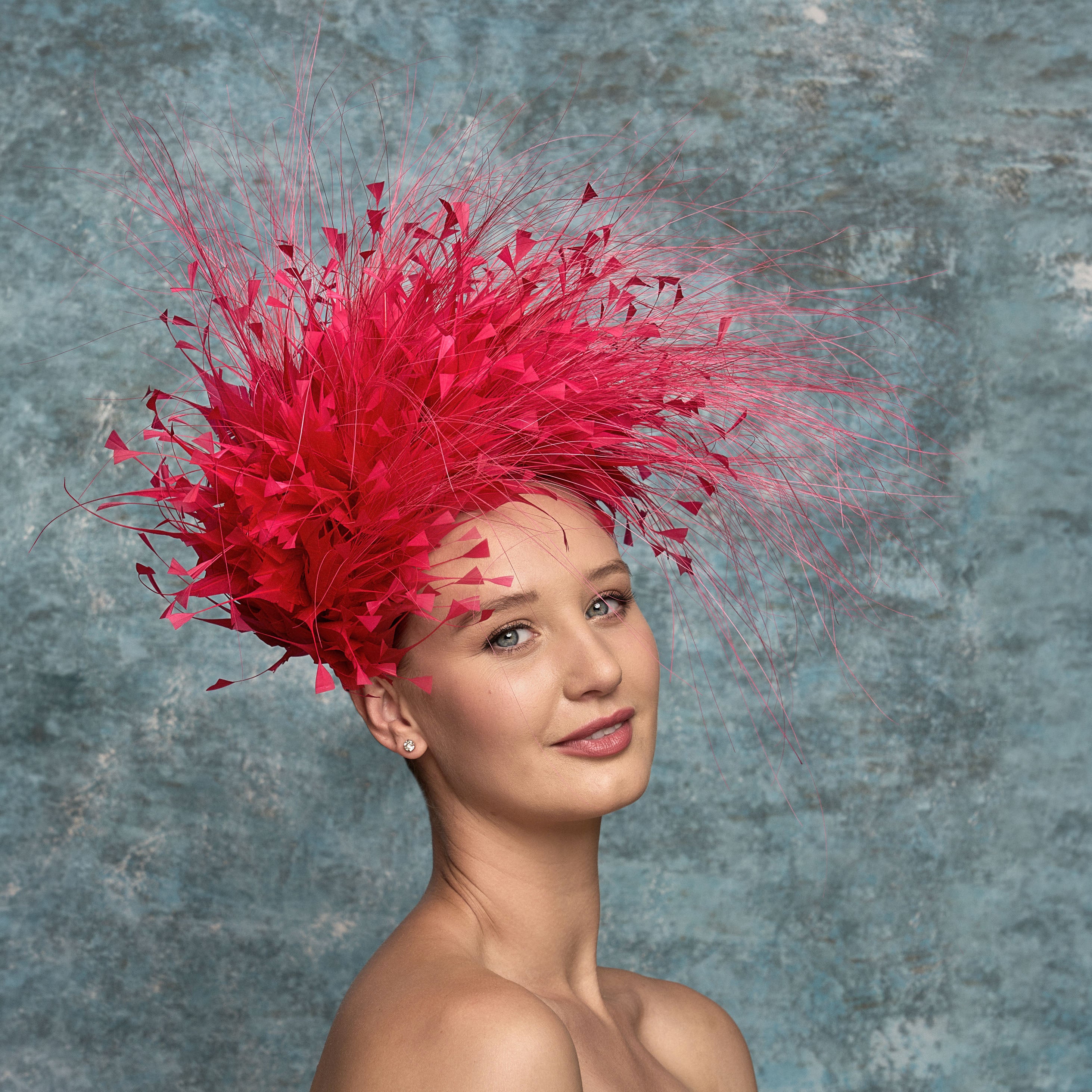 Woman wearing a vibrant pink feathered headpiece against a textured gray background
