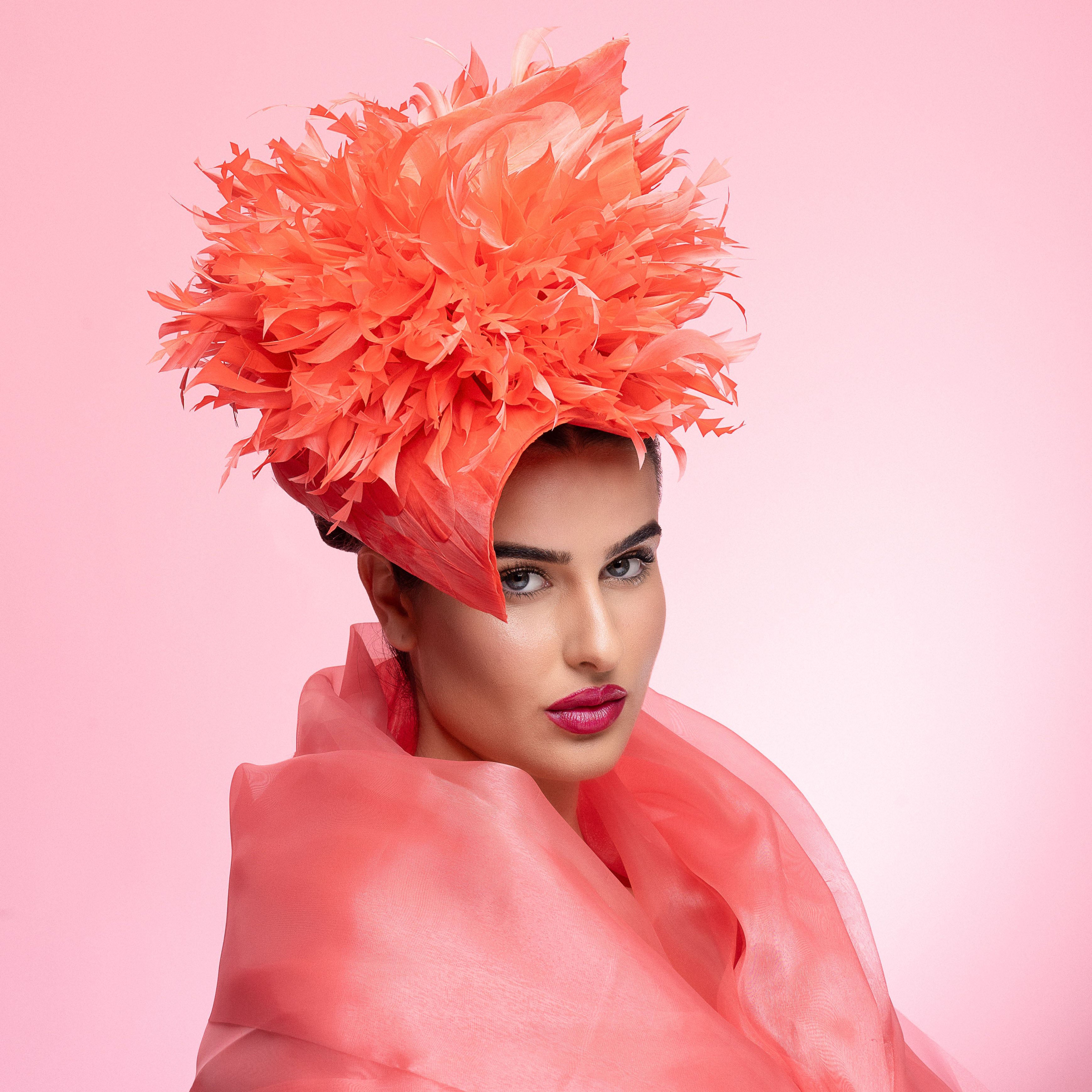 Woman wearing a vibrant orange feathered headpiece against a pink background