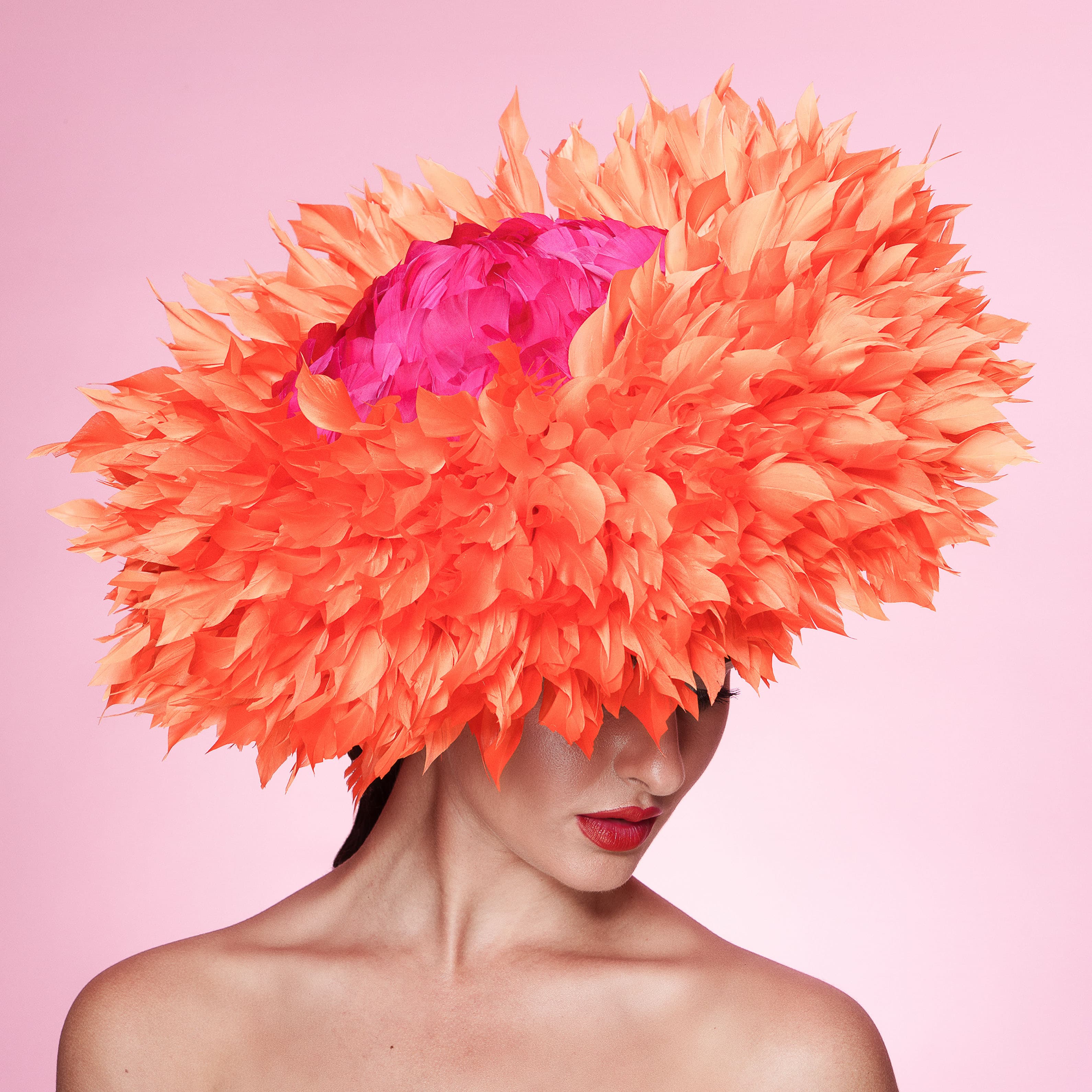 Woman wearing a large orange feathered hat with a pink center on a pink background