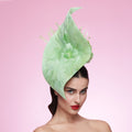 Woman wearing a large green feathered hat against a pink background