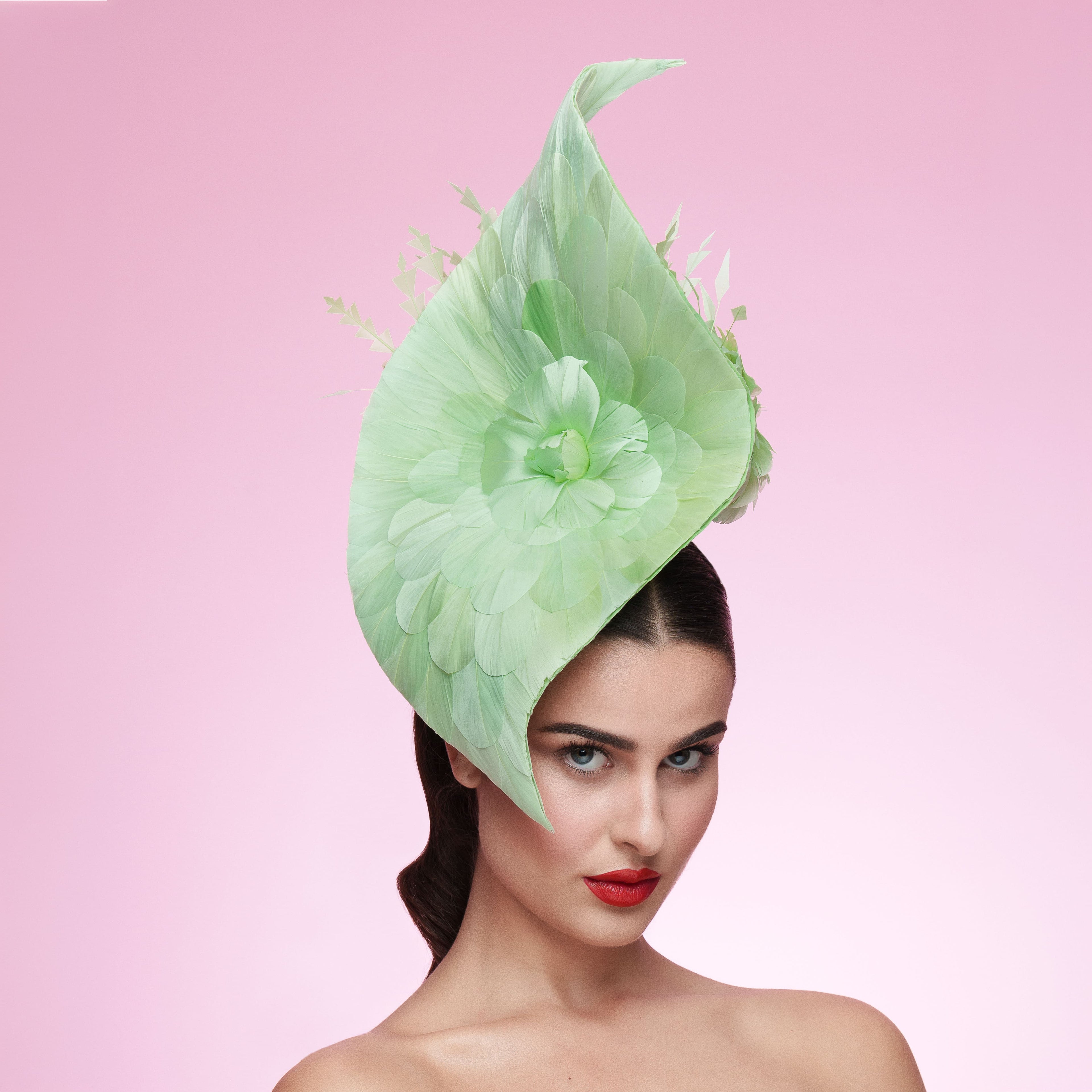 Woman wearing a large green feathered hat against a pink background