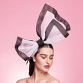 Woman wearing a large decorative headpiece on a pink background